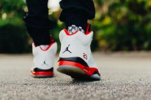 Eine Person, die weiße, schwarze und rote Air Jordan 5 Schuhe trägt